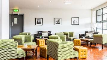 A hotel lobby with green patterned furniture, a fire alarm, and framed pictures on the wall.
