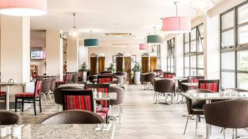 A spacious restaurant with multiple tables and chairs, large windows, and hanging pendant lights.