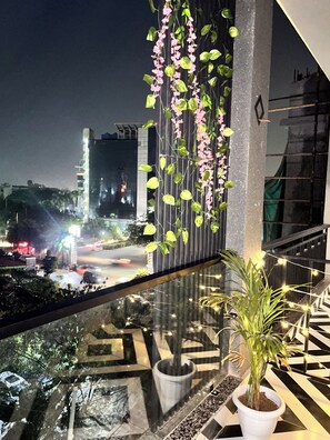 Ein Balkon mit Blumentopf, Geländer und Blick auf eine nächtliche Stadtansicht.