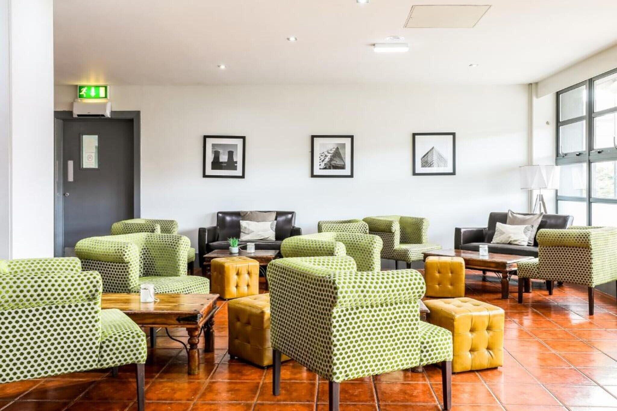 A hotel lobby with green patterned chairs, a wooden coffee table, and a tiled floor.