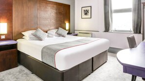 A hotel room with a large bed, bedside tables, a desk, and a window with curtains.