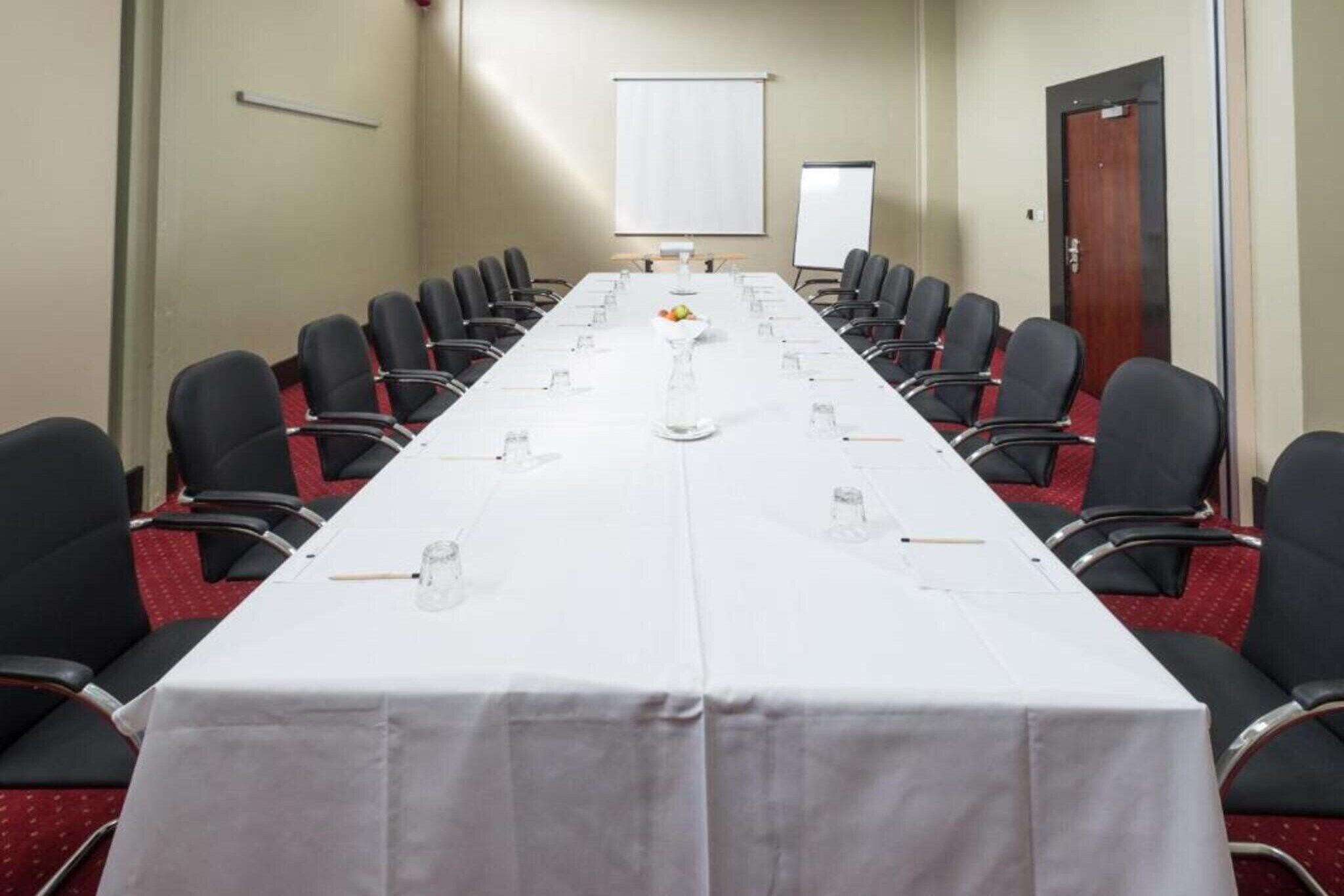 Een vergaderzaal met een lange tafel, stoelen, een projectiescherm en een whiteboard.