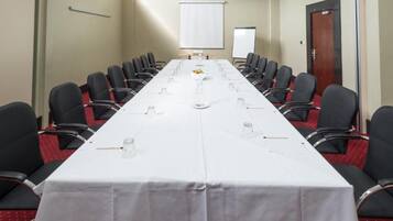 Een vergaderzaal met een lange tafel, stoelen, een projectiescherm en een whiteboard.