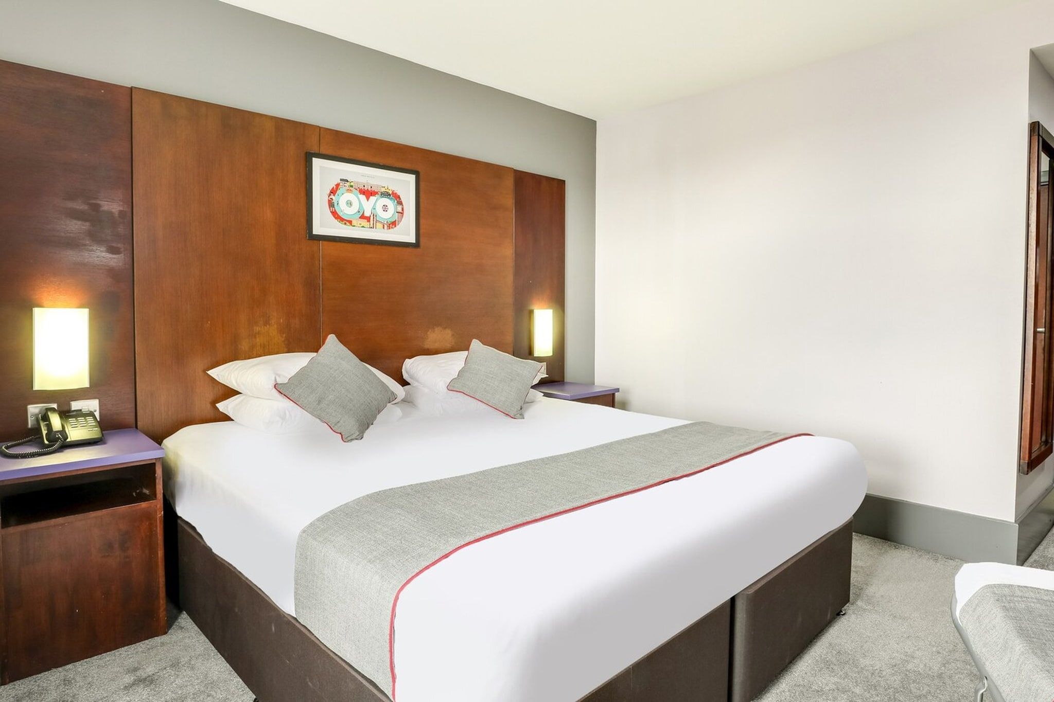 Une chambre d’hôtel avec un grand lit, une tête de lit en bois, des lampes de chevet, un téléphone et un tableau encadré au mur.