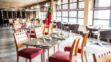 A spacious dining area with multiple tables and chairs, large windows, and a potted plant.