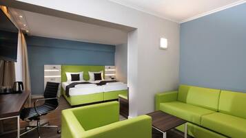 A modern hotel room with a bed, green sofa, a desk, and a chair.