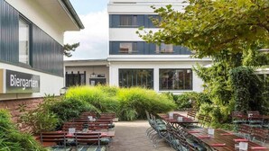 Zona d'aigües obertes amb taules i caires, envoltada de vegetació i un edifici amb un rètol que diu 'Biergarten'.