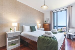 A hotel room with a bed, bedside tables, a dresser, a chair, and a large window with a view. - Aurora Atlantic Apartment by Atlantic Holiday (Caniço)