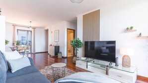 A modern living room with a sofa, TV, glass coffee table, and a dining area with chairs and a table. - Aurora Atlantic Apartment by Atlantic Holiday (Caniço)