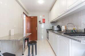 A kitchen with white cabinets, a granite countertop, a sink, a stove, and a door with a sign. - Aurora Atlantic Apartment by Atlantic Holiday (Caniço)