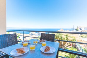 A balcony with a table set for breakfast, including croissants and orange juice, overlooking a coastal view. - Aurora Atlantic Apartment by Atlantic Holiday (Caniço)
