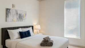A neatly made bed with pillows, a bedside lamp, and rolled towels. - Upscale 2BR Apt | Rooftop Deck + Fitness U14 (Birmingham)