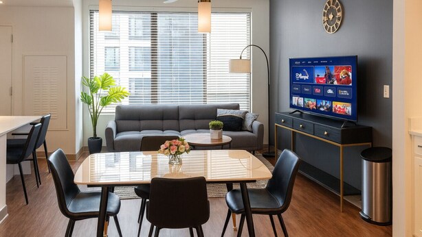 A modern living room with a sofa, dining table, chairs, a TV, and a plant. - Upscale 2BR Apt | Rooftop Deck + Fitness U14 (Birmingham)