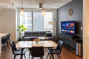 A modern living room with a sofa, dining table, chairs, a TV, and a plant. - Upscale 2BR Apt | Rooftop Deck + Fitness U14 (Birmingham)