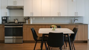 A modern kitchen with stainless steel appliances, white cabinets, and a marble dining table with chairs. - Upscale 2BR Apt | Rooftop Deck + Fitness U14 (Birmingham)