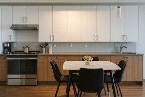 A modern kitchen with stainless steel appliances, white cabinets, and a marble dining table with chairs.