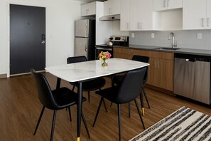 A modern kitchen with a white countertop, stainless steel appliances, and black chairs around a white table.