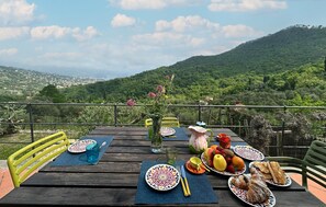 Une table dressée à l’extérieur, avec des assiettes remplies de nourriture, un vase de fleurs et une vue imprenable sur les montagnes.