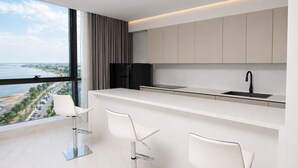 A modern kitchen with a large window, white bar stools, and a view of a body of water.
