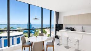 A modern kitchen with a view of the sea, a dining area with a round table, and a bar with stools.
