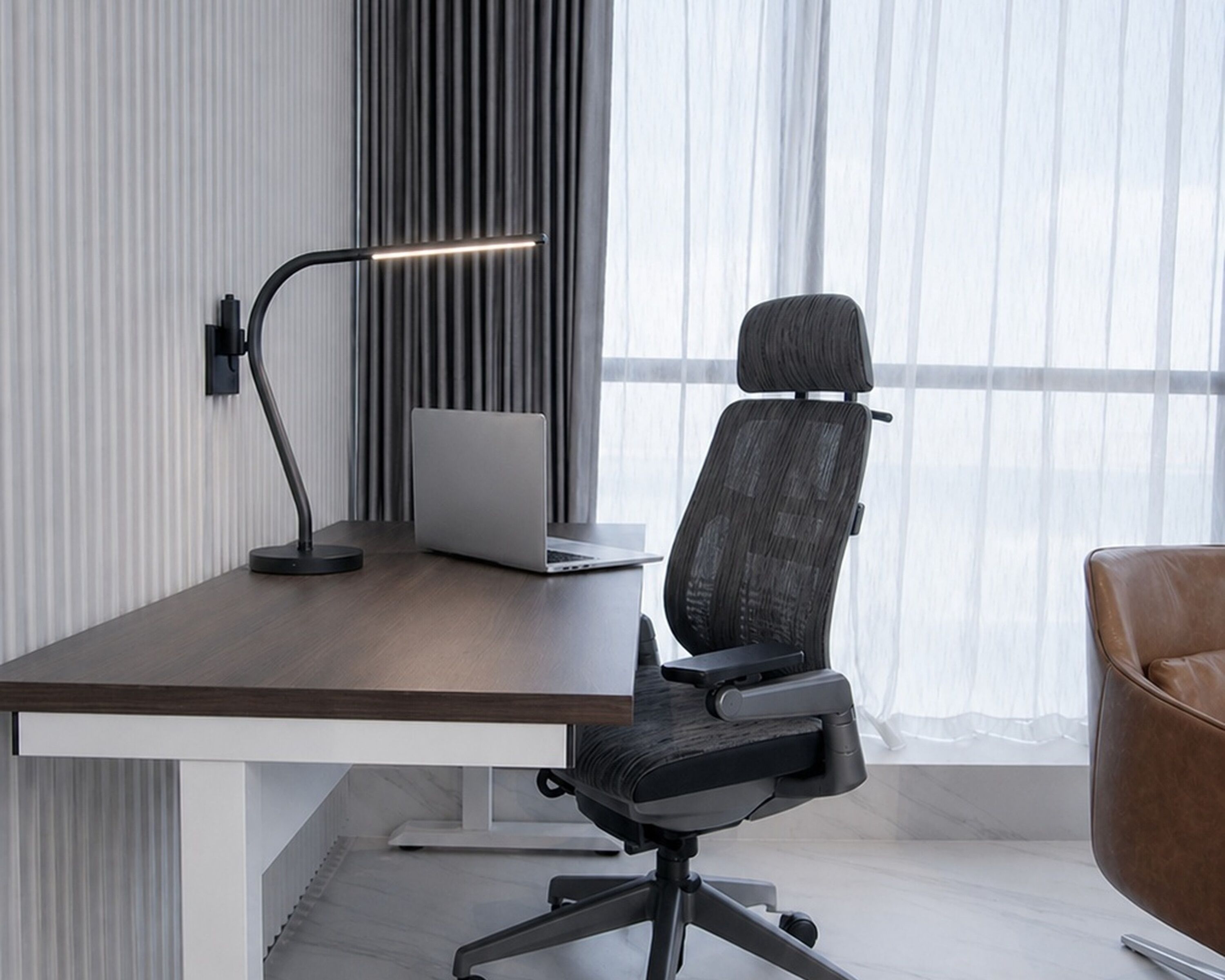 Un escritorio moderno con una computadora portátil, una silla y una lámpara de escritorio.