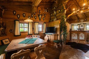 A rustic wooden interior with a dining table, chairs, a television, and antler decorations.