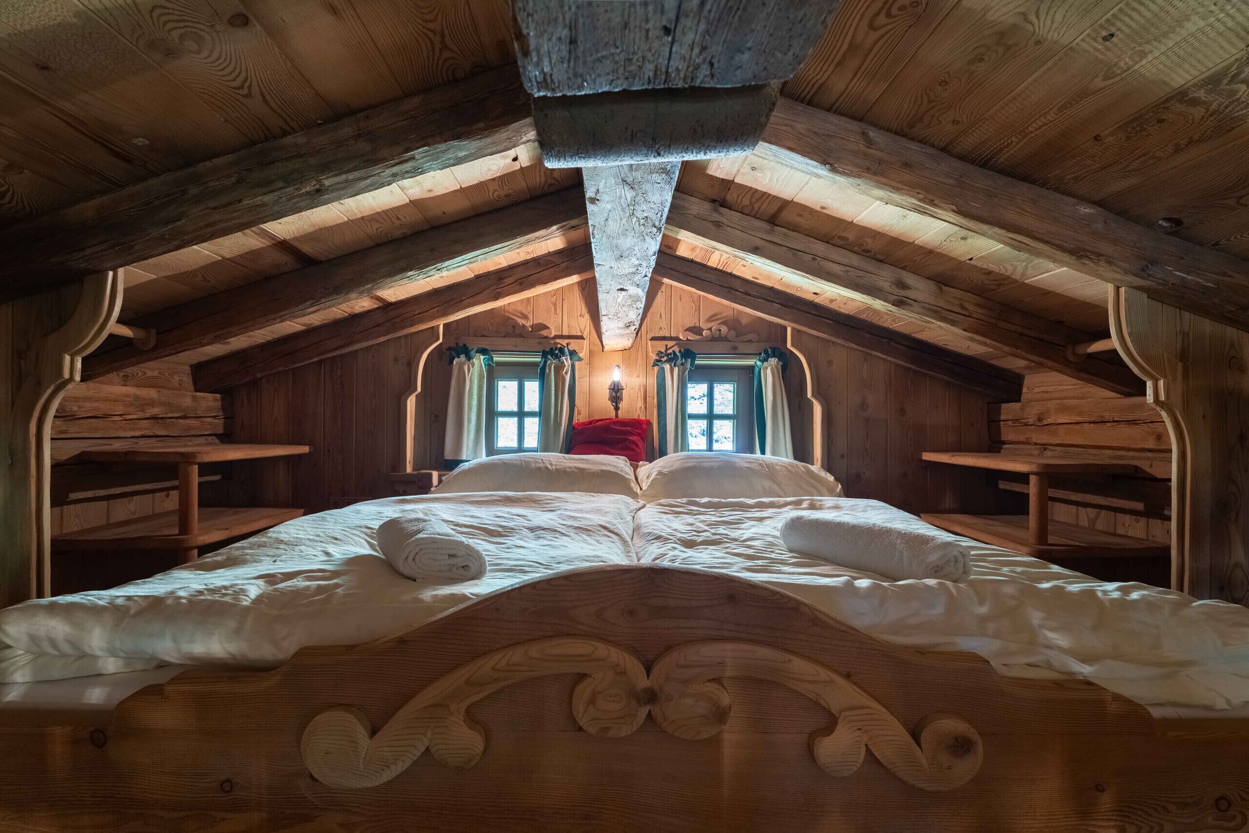 Een houten slaapkamer op zolder met een bed, twee ramen en een schuine kap.