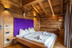 Ein Schlafzimmer einer Holzhütte mit einem Bett, einem violetten Kopfteil, einem aufgehängten Tierkopf und einem kleinen Regal.