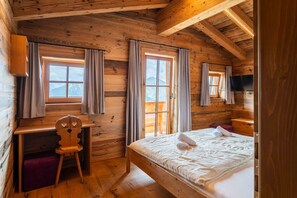 A wooden cabin room with a bed, a desk, a chair, and a TV.