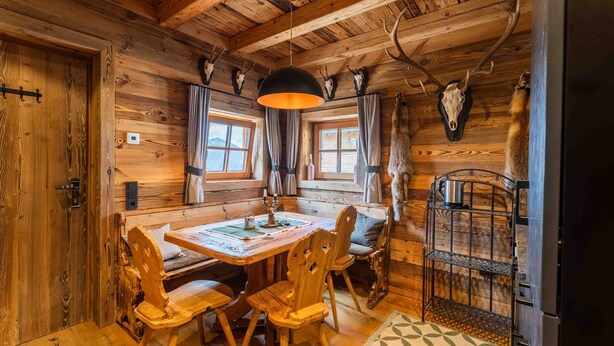 A wooden cabin interior with a dining table, chairs, a hanging light fixture, and deer antlers mounted on the wall. - Panorama Alm Chalet - Jägersruh Zwei, Ski-in / out & mountain view (Saalbach)