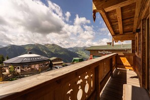 A wooden balcony overlooking a mountain landscape with a restaurant and a mountain hut.