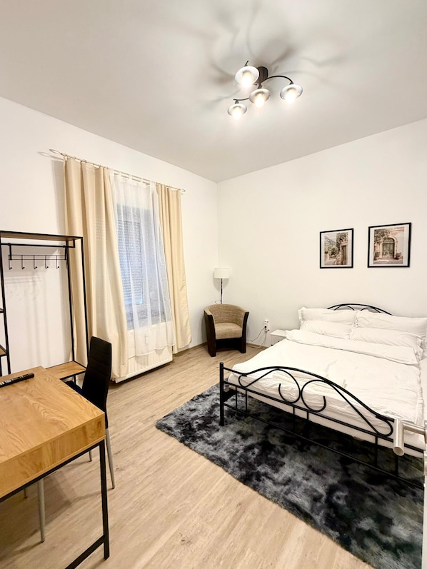 Ein Schlafzimmer mit einem Bett, einem Schreibtisch, einem Stuhl, einer Lampe und zwei gerahmten Bildern an der Wand.
