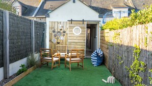 Eine kleine Holzhütte mit Tisch und Stühlen, einem Holzzaun und einem Gartenbereich mit Kunstgrashalm.