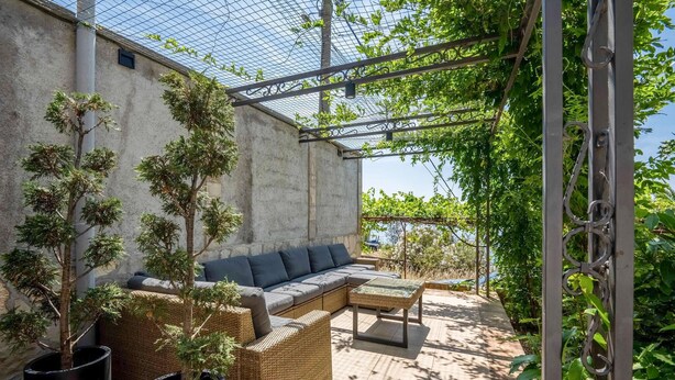 Un'area salotto esterna riparata, con divano, poltrone, piante in vaso e una pergola.