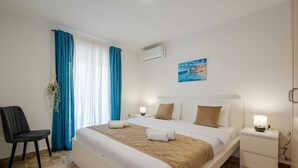 Una camera d'albergo con un letto, una sedia, un comodino e un condizionatore d'aria a muro.