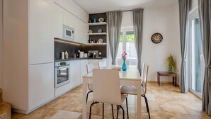 Una cucina moderna con mobili bianchi, un tavolo da pranzo con sedie, una sveglia al muro e una finestra con tende.