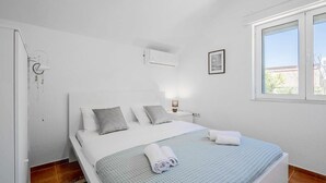 Une chambre à coucher comprenant un lit, une lampe de chevet, un appareil de climatisation, une fenêtre et un tableau encadré accroché au mur.