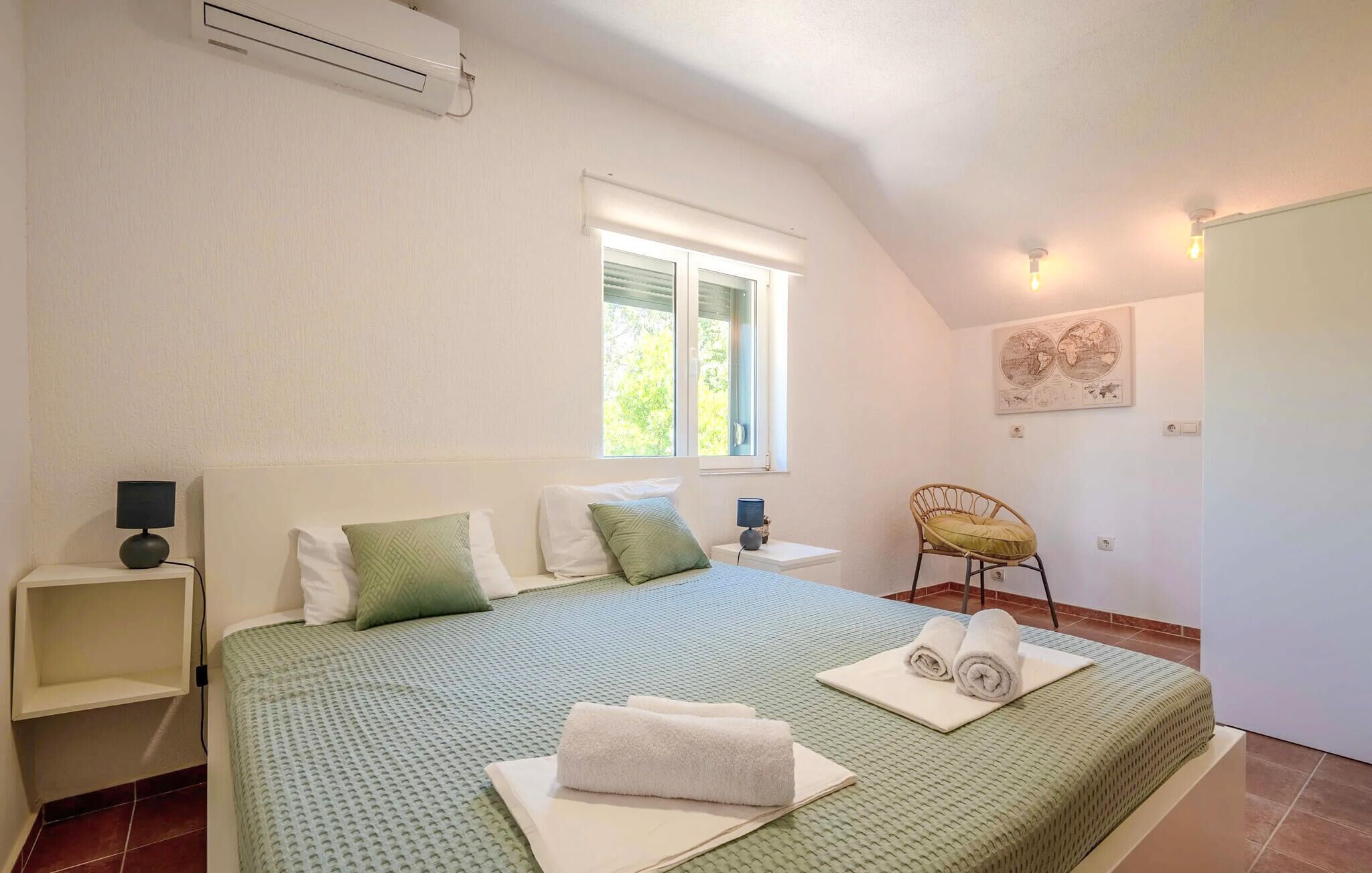 A bedroom with a bed, a window, a chair, a lamp, and a wall-mounted air conditioner.