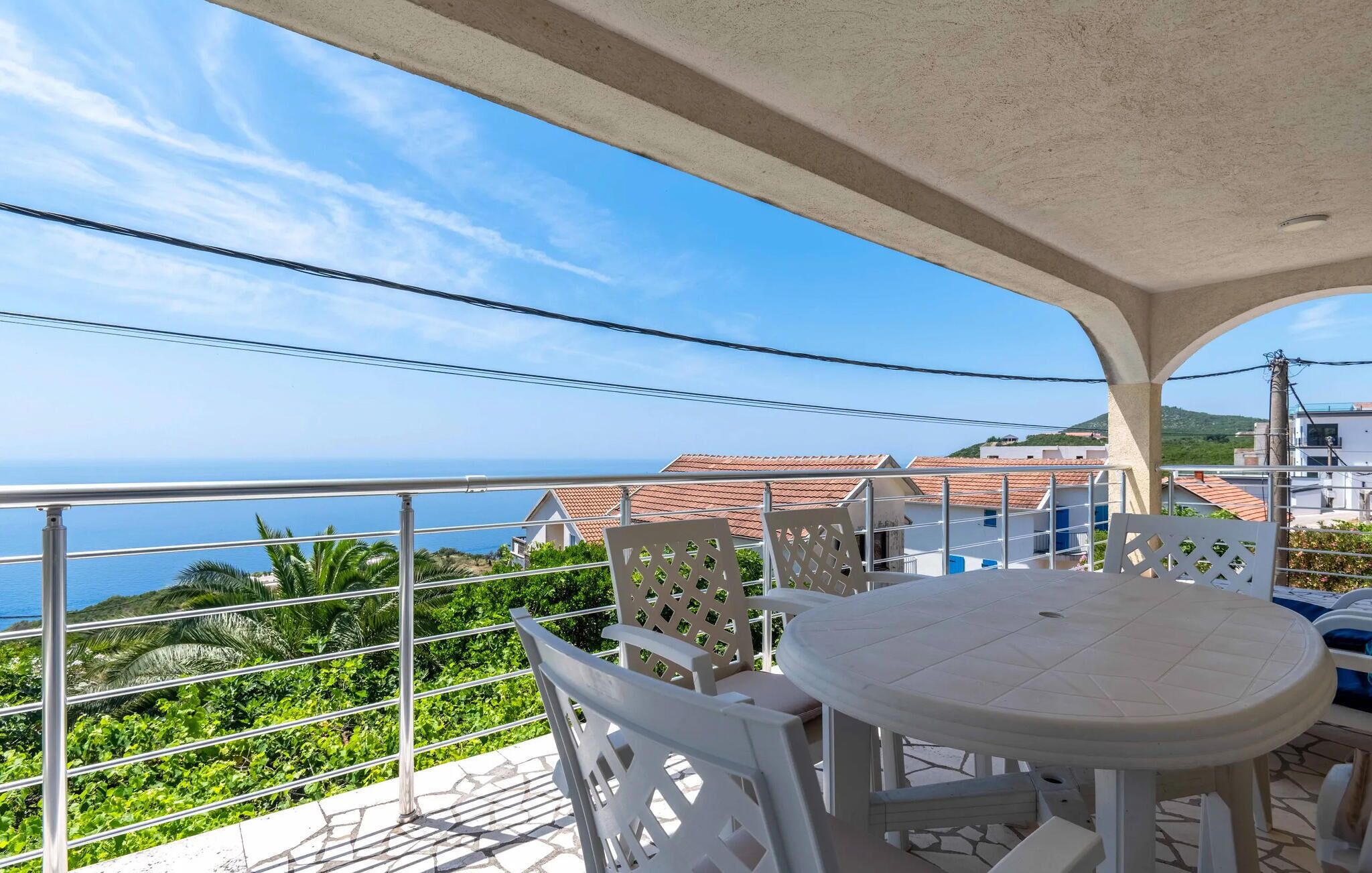 Ein Balkon mit Tisch und Stühlen, der auf eine Küstenlandschaft mit Häusern und Grünblicken blickt.