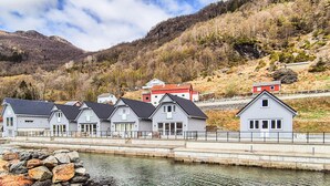 A row of houses by a calm water body with a mountainous backdrop.