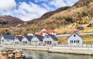 A row of houses by a calm water body with a mountainous backdrop. - 3 bedroom nice home in Sandeid (Sandeid)