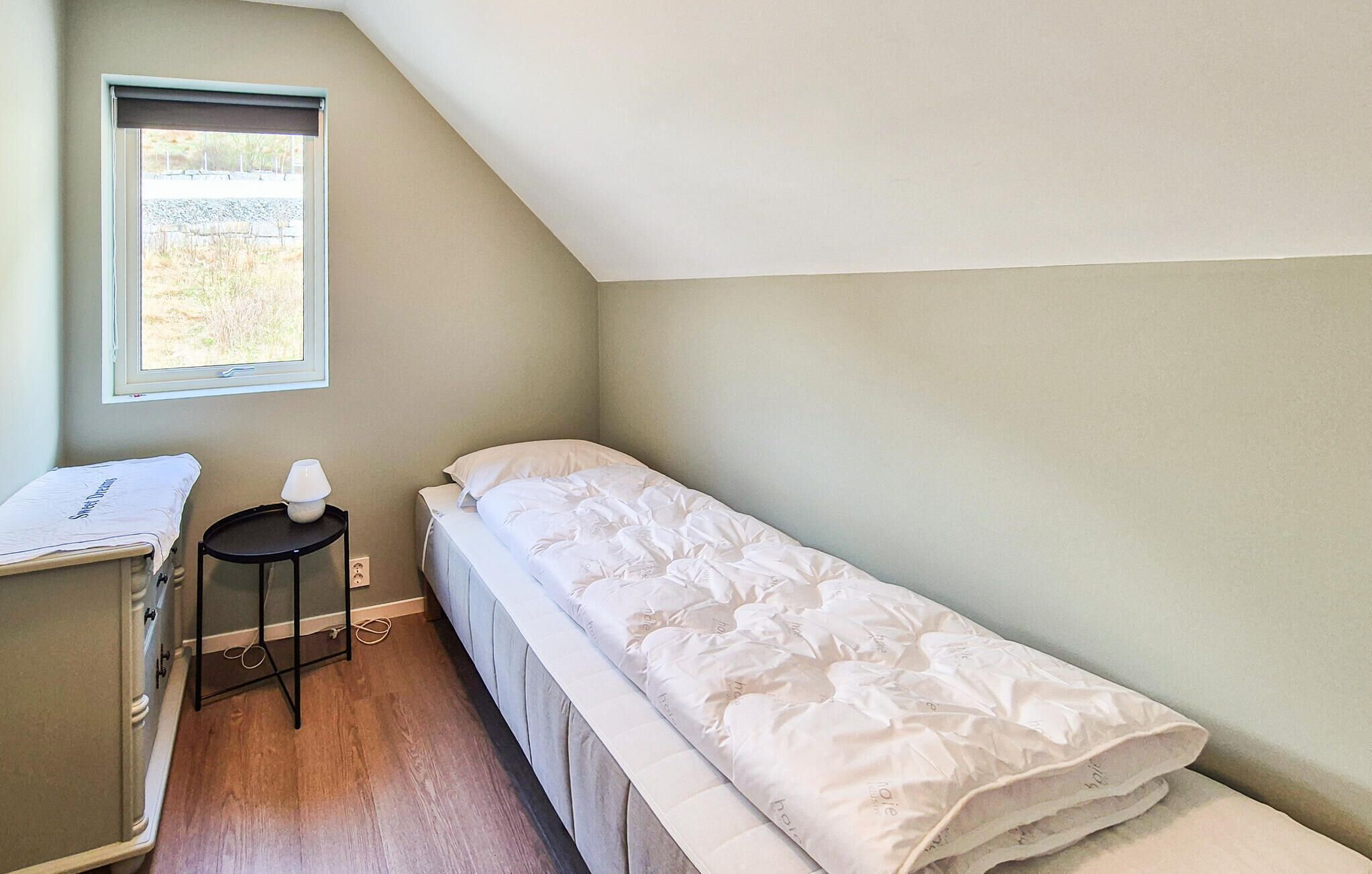 Een kleine kamer met een enkel bed, een raam, een bureau en een stoel.
