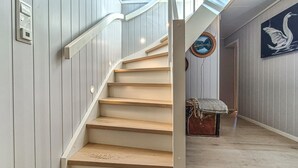 Un escalier avec des marches en bois et des rampes blanches, menant à une pièce où est accrochée, au mur, une image encadrée représentant un cygne.