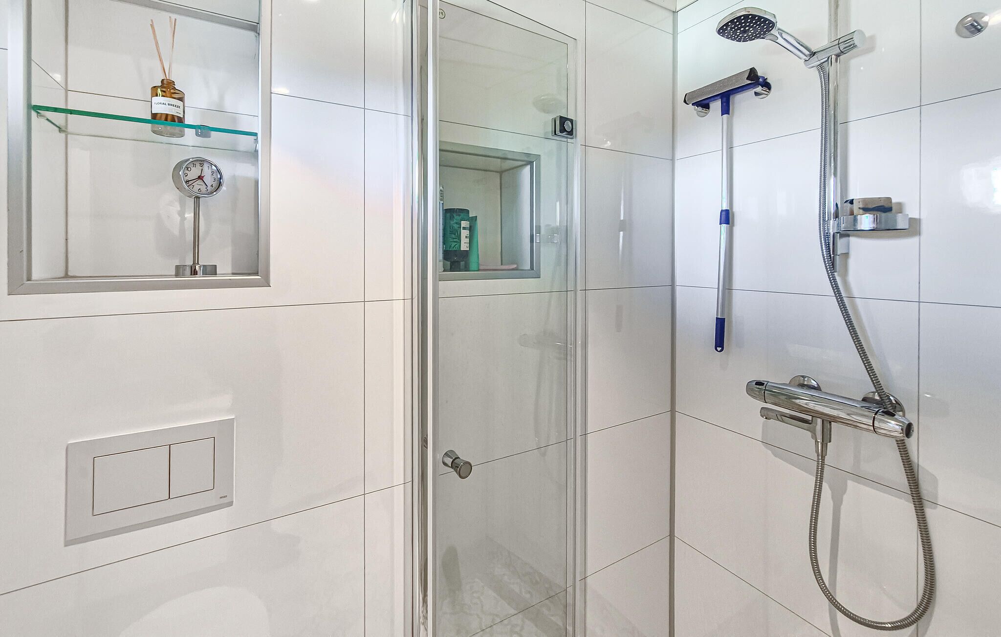 Een moderne badkamer met een douchecabine van glas, een handdouche en een kraan op de muur.