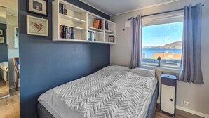 Une chambre à coucher avec un lit, une fenêtre avec des rideaux, une bibliothèque et une vue sur la mer.