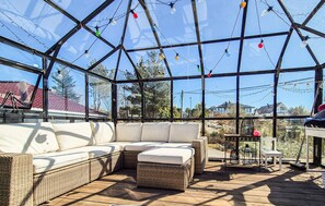 Un patio con paredes de vidrio, muebles de mimbre e iluminado con guirnaldas de luces.