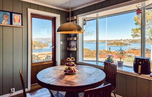 Un comedor con una mesa redonda de madera, una lámpara colgante y vista a un lago.