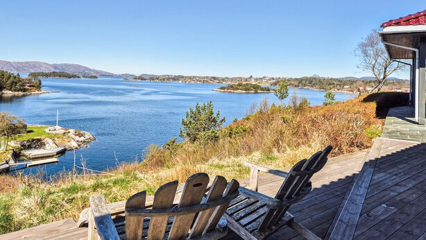 Eine Holzterrasse mit Blick auf einen See, mit Stühlen und einem kleinen Steg.
