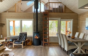 L’intérieur d’une cabane en rondins comprend une cheminée, un plancher en bois, un coin repas et une mezzanine avec balcon.