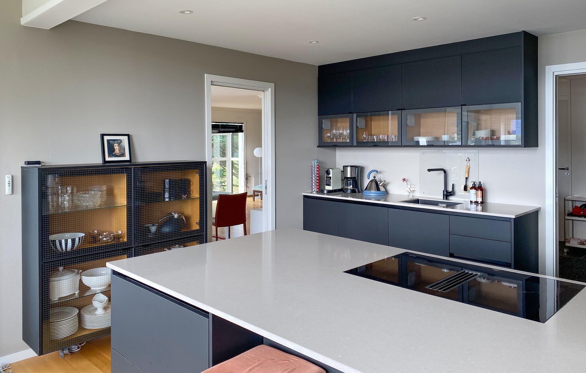 A modern kitchen with a central island, dark cabinetry, and a glass-fronted display cabinet.